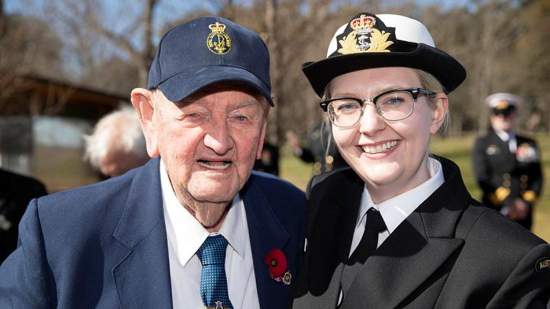 A military woman stands with an elderly man with a poppy pinned to his blazer.