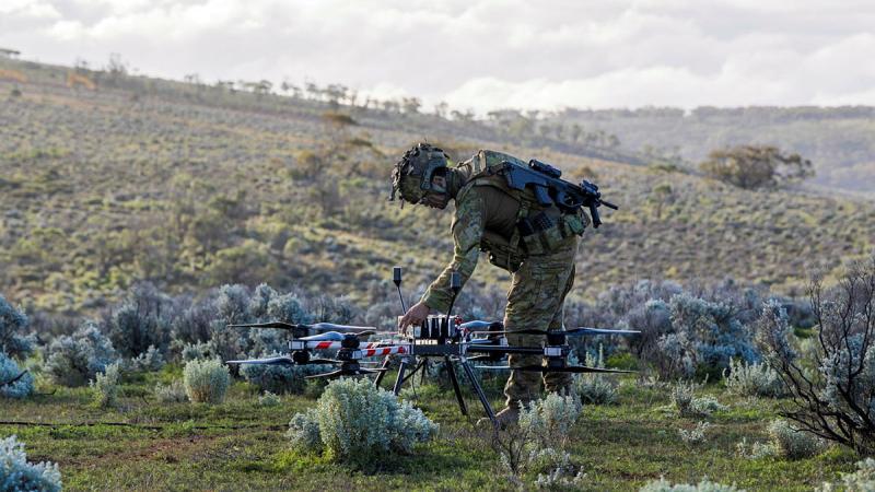 A soldier adjusts a large drone, positioned in an open field.
