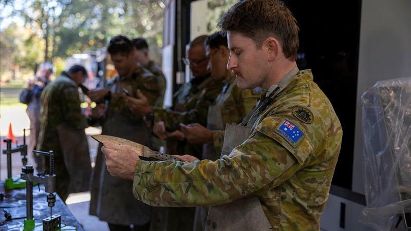 A military member inspects a blade in a workshop.
