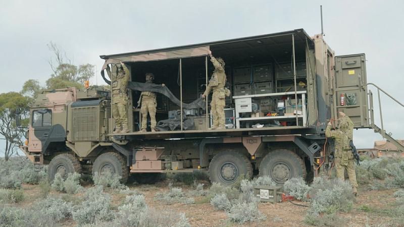 Soldiers stand in a fitted out truck with the side canvas side wall open.