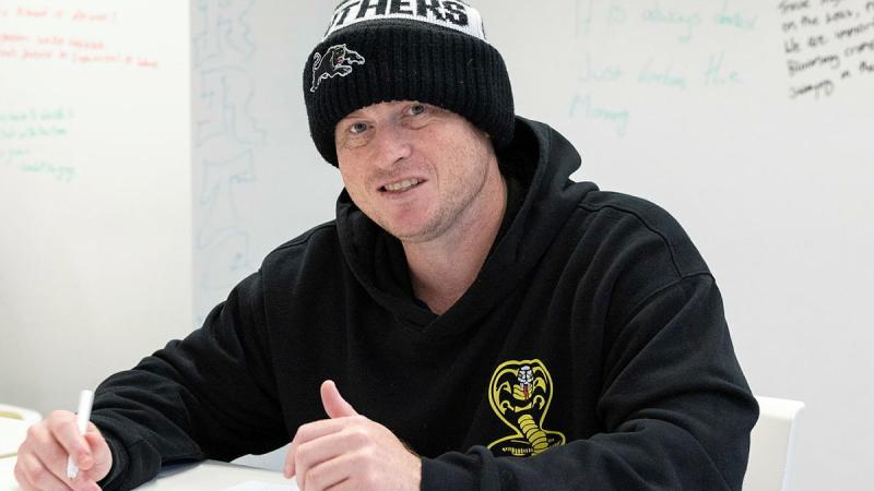 A man in a beanie and black jumper sitting at a table drawing.