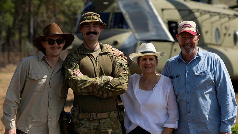 A man in uniform stands with three other people in casual clothes in front of an Army helicopter.