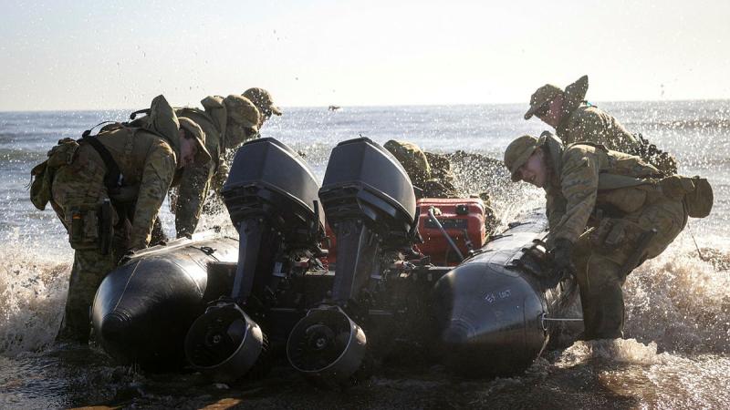 Several military personnel move a boat from the shore out to sea.