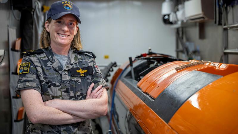 A smiling sailor stands with her arms crossed next to a bright orange piece of equipment.