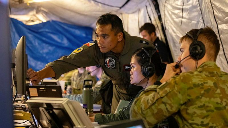 Several military personnel work on a shared screen inside a makeshift building.