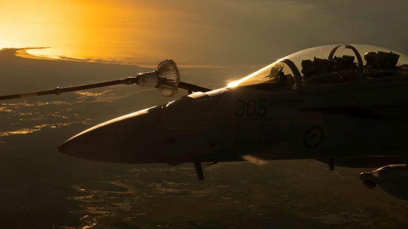 An aircraft in flight over a coastal area at sunrise.