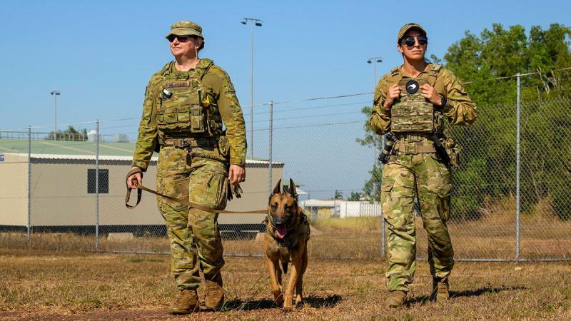 Two military women lead a working dog around a base.