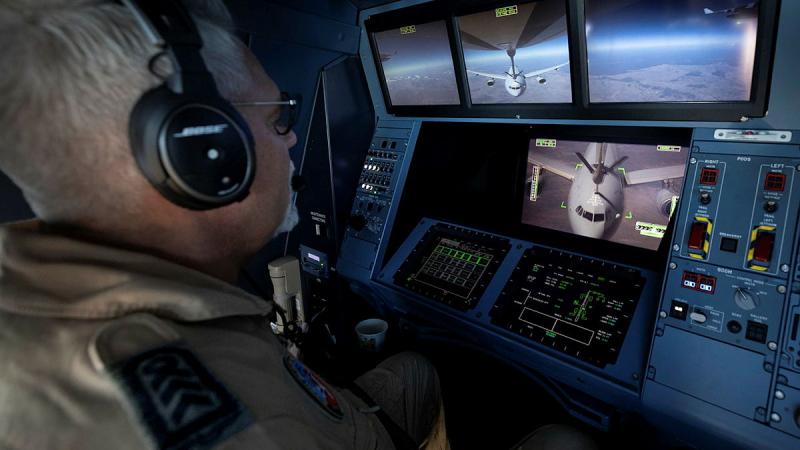 A military member looks at several screens of aircraft in flight.