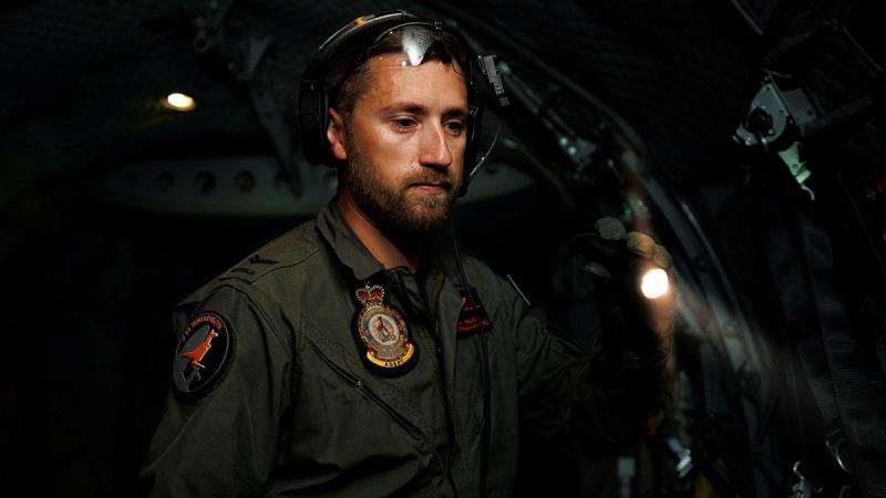 A military member searches in the dark of a cabin with a flashlight.