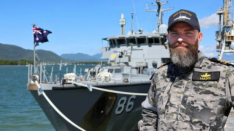 A military man stands before a docked ship.