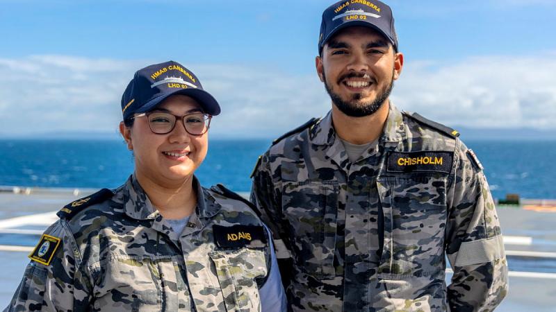 Two sailors stand on the flight deck of a ship at sea.