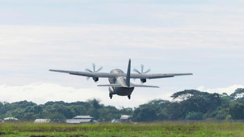 An aircraft flies above grass and into the sky.