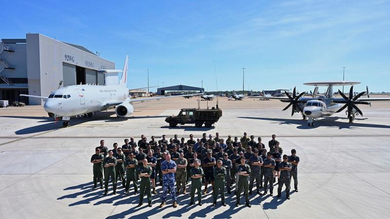 A group of people stand on the tarmac in front of a plane.