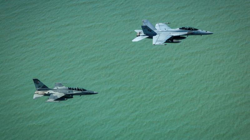 Two aircraft fly over a body of water.