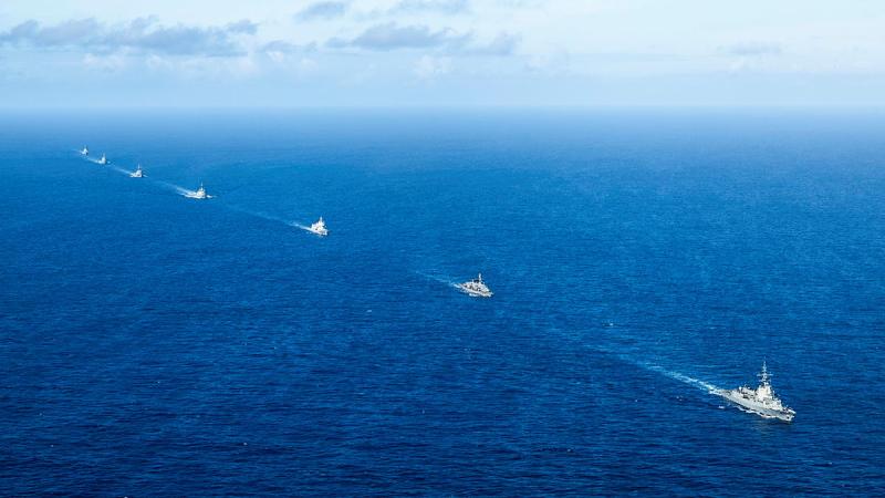 Seven ships sail in a line in a deep blue ocean.