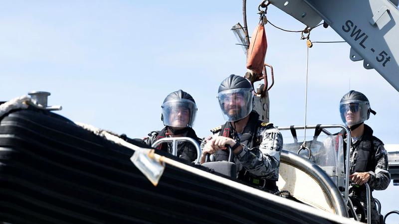 Three military men aboard a small sea vessel.