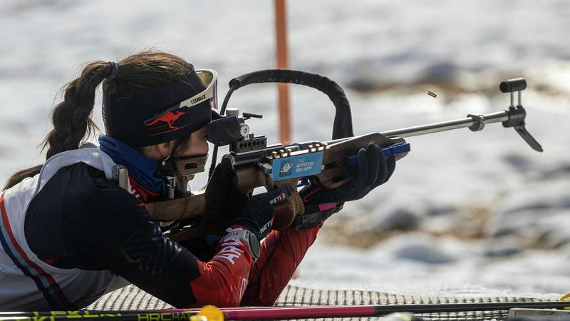 A woman holds a rifle and takes aim in snow covered terrain.