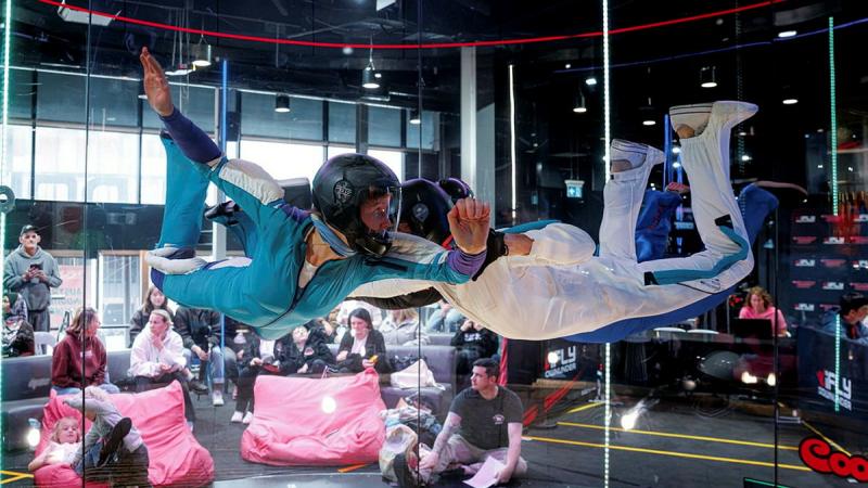 Two people perform an indoor skydiving formation.