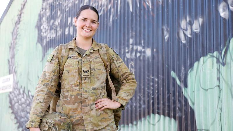 A woman in uniform stands with her back to a wall covered in street art.
