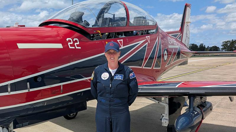 A female pilot stands in front of a small red plane.