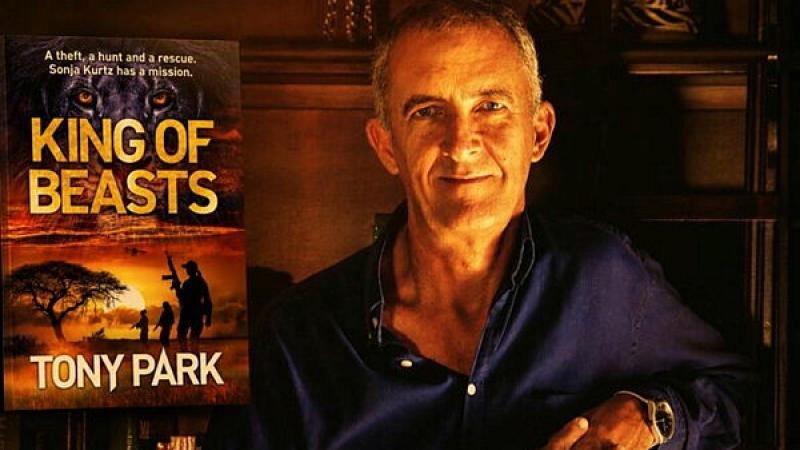 A man sits, bathed in warm light, with a poster of a book called 'King of Beasts' next to him.