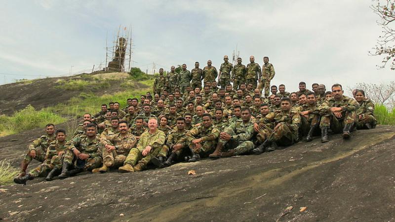 A large group of military personnel sit on a rocky cliffside.