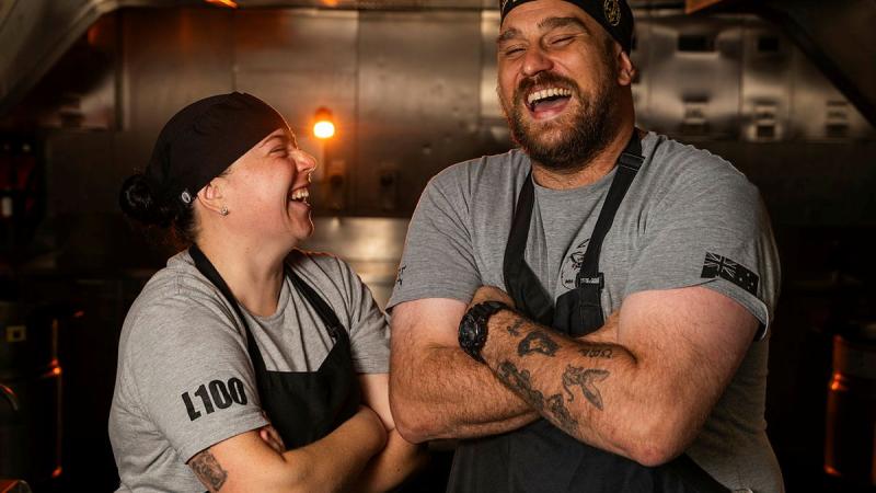 Two chefs laugh together in a kitchen.