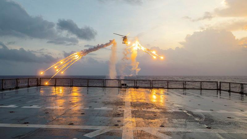 A helicopter fires flares behind a ship.