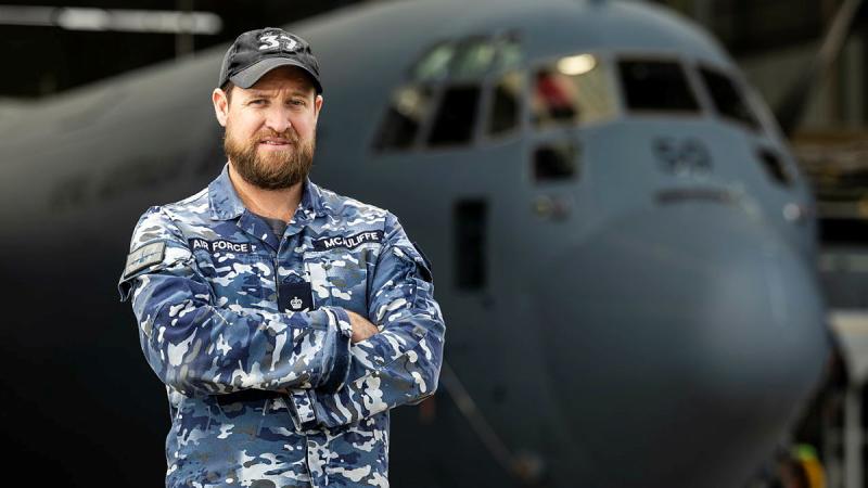 A portrait of Flight Sergeant Luke McAuliffe in uniform, with his arms crossed in front of a RAAF aircraft.