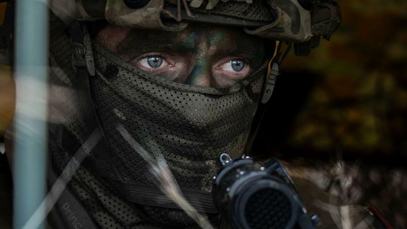 A soldier in full military gear waits in hiding.