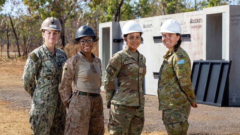 Four women military members wearing hard hats stand out in the bush.