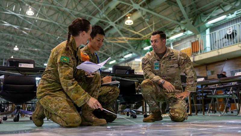 Three military members work together while knelt on the floor.