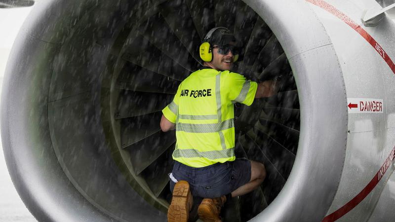 A man in yellow Air Force branded clothing and ear protection sits inside a cylindrical part of an aircraft .