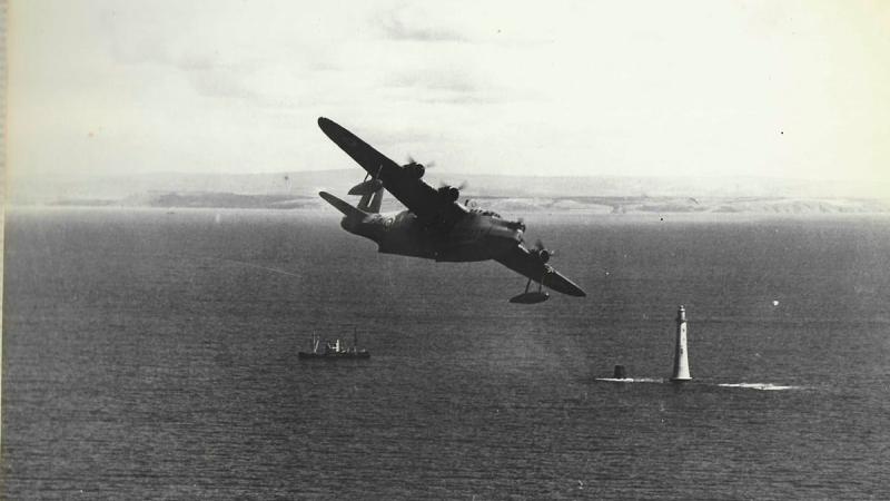A black and white photo of an aircraft flying over an ocean.