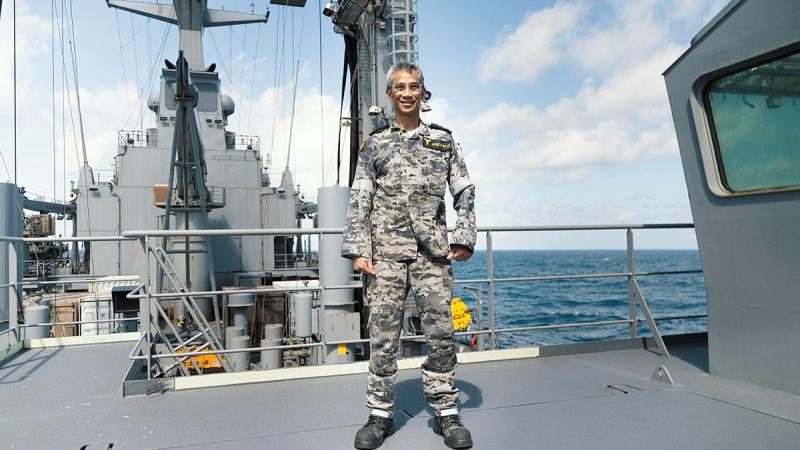 A man in Navy uniform stands on the deck of a ship at sea.