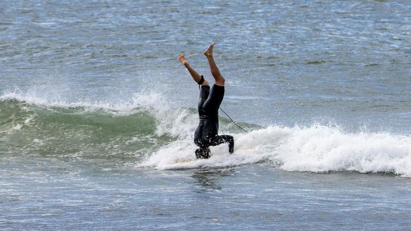 A male surfer does a headstand while surfing in the ocean.