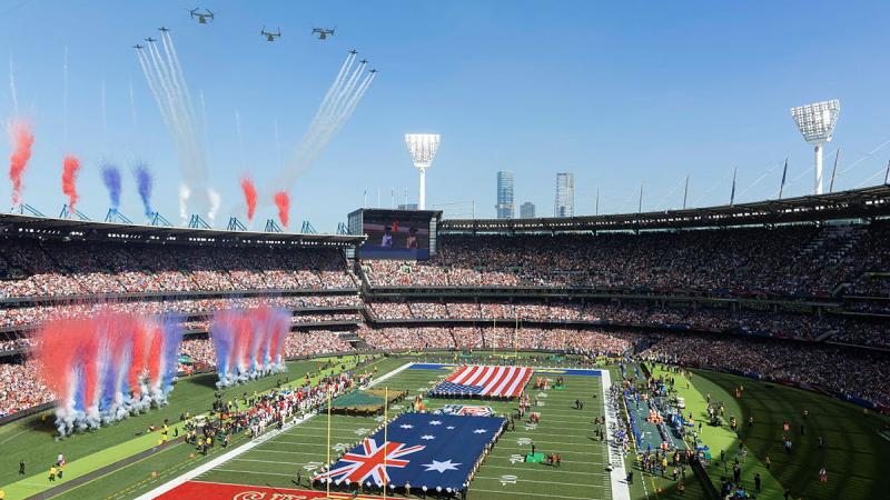 A filled out stadium with US and Australian flags, confetti explosions and aircraft flying in formation.
