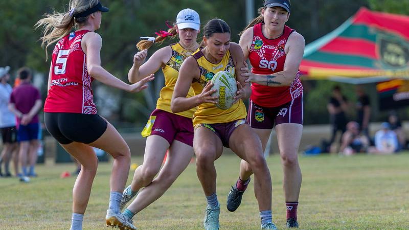 Four women compete in a sports game using a rugby ball.
