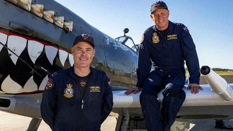 Two aviators stand and sit near and on an aircraft.