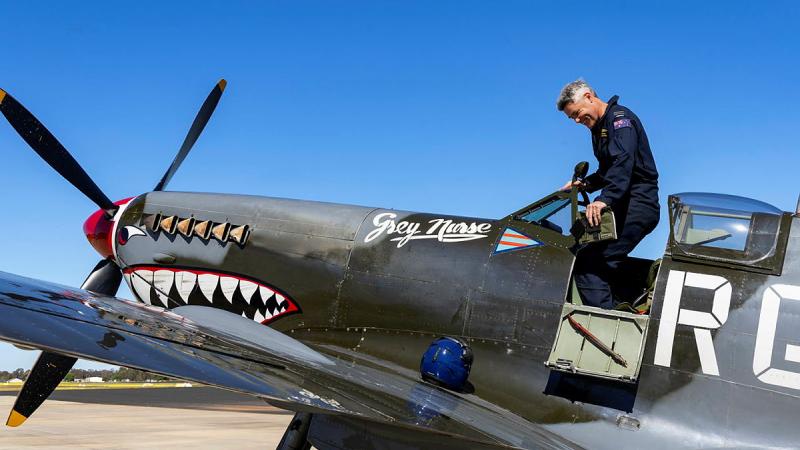 A man stands up to exit from the cockpit of a small aircraft that has eyes and teeth painted on it.