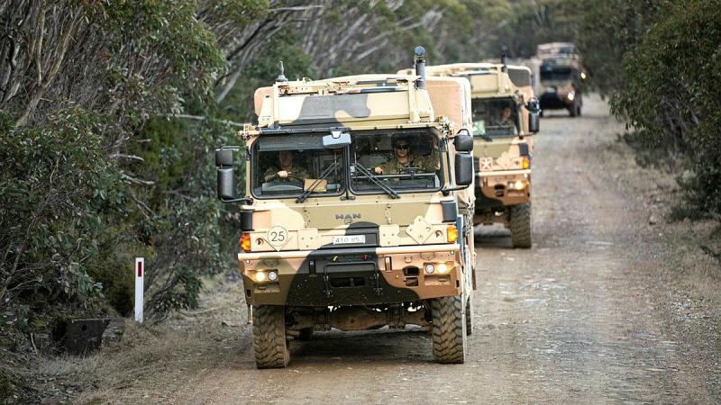 A convoy of Army trucks drive along a dirt road.