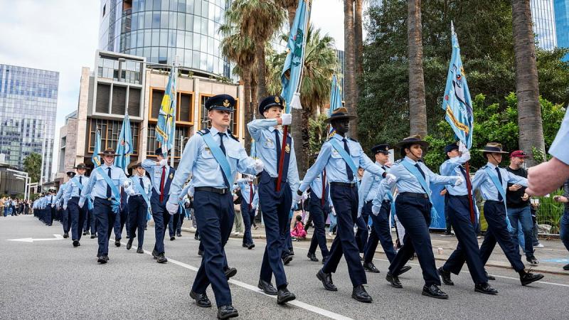 A large formation of young military personnel march through a city.