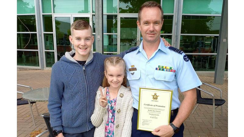 A military officer holds a certificate of promotion next to their two children.