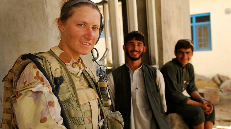 A woman in military uniform stands near two men in traditional Afghan clothing.