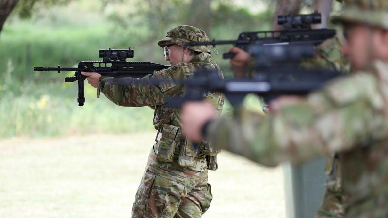 Two soldiers aim guns outside.