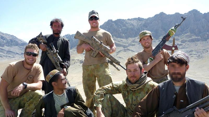 A group of armed soldiers and civilians in a dry, mountainous region.