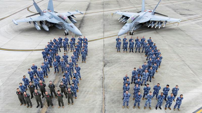 A group of military personnel use their bodies to spell 82 in front of two aircraft.