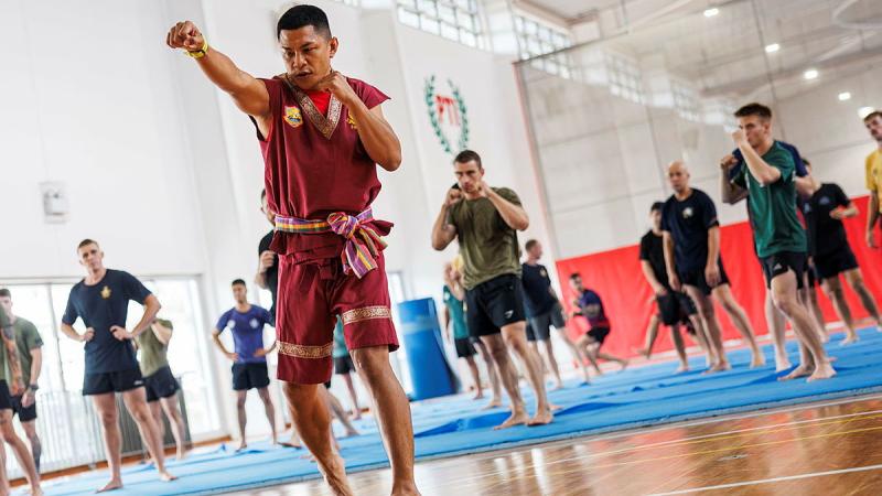 A Thai Army martial artist faces the camera and throws a punch in front of his class.