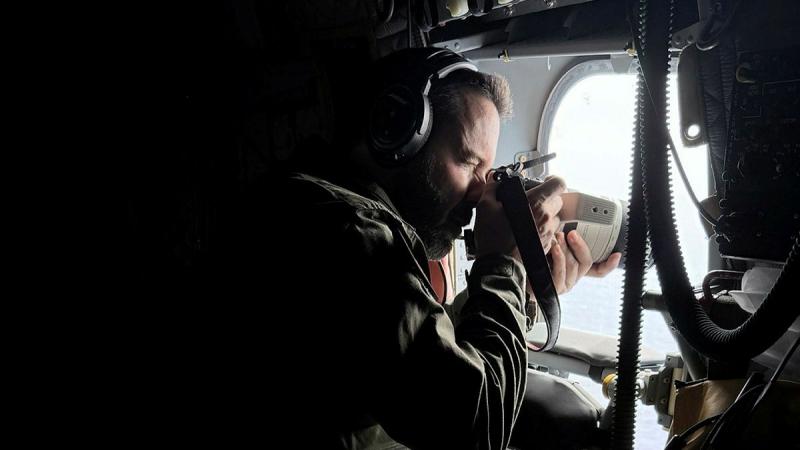 A military man takes a photo out the window of an aircraft.