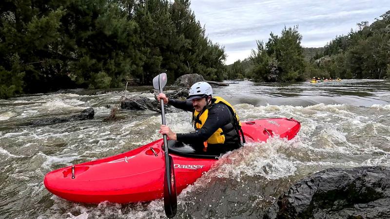 A man in a red kayak holds a paddle as he moves through rushing water.
